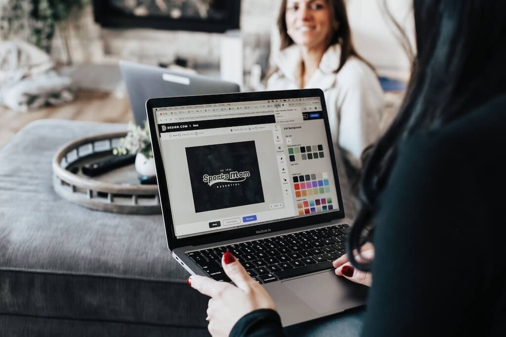Sports Mom Essential founders Vivianne Bolen and Jiji Radzieski sitting with laptops in family room. Close up of laptop with Sports Mom Essential logo